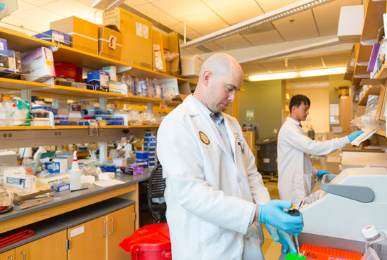 ucsd faculty research wearing white lab coat holding beaker in lab